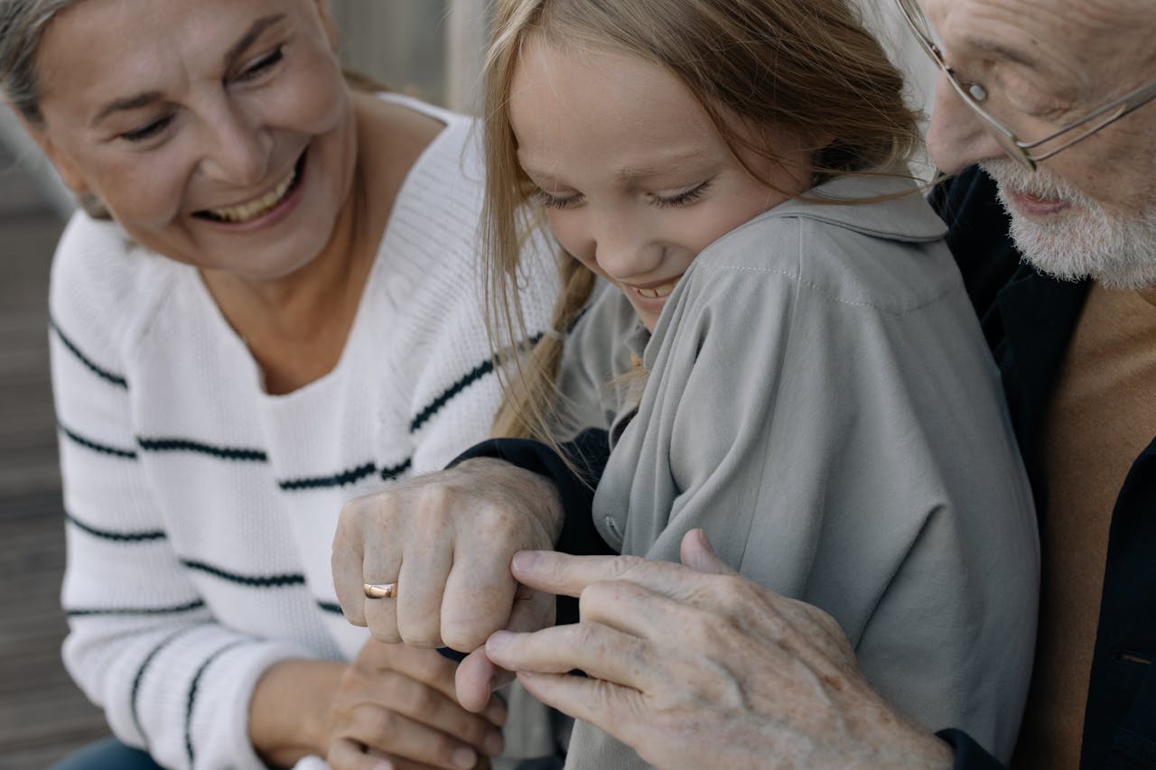 Smiling grandparents sharing a joyful moment with their granddaughter outdoors.